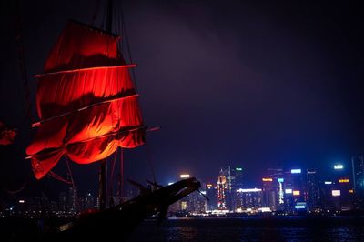 Illuminated ship canvas in sea by modern buildings at night