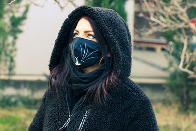 Woman wearing hood and mask looking away while standing outdoors