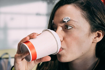 Close-up of young woman with speech bubble on face drinking coffee