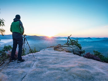 Artist with camera and tripod watch sunrise on rocky summit. misty  saxon switzerland national park.