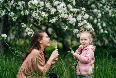 Mother and daughter with dandelions blooming apple trees