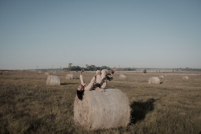 Young man lying down on hay bale at agricultural landscape