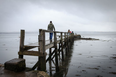 People on wooden pier over sea against sky