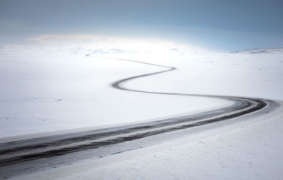 Empty curvy country road going through desert snowy terrain in cold winter day with blue sky in iceland