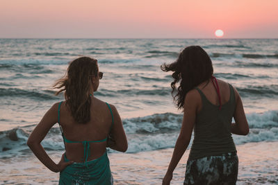 Rear view of women standing at beach during sunset