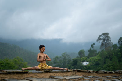 A young indian cute kid doing yoga in the mountains,wearing a dhoti