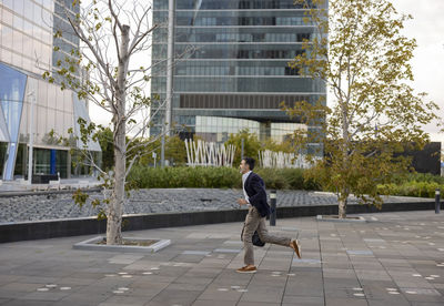 Businessman running on footpath in front of office building