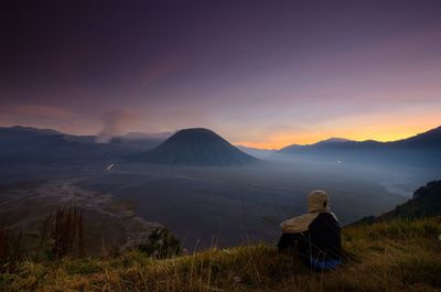 Rear view of person looking at mountains against sky during sunset