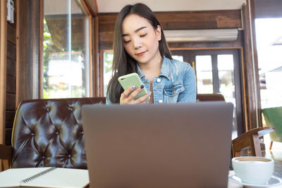 Young woman using phone while sitting on table