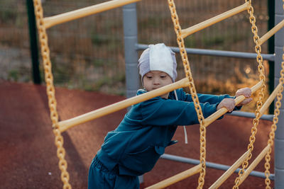 Little boy with down syndrome holds onto the steps of a metal suspended ladder