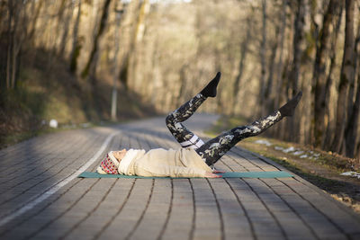 Beautiful young woman doing hatha yoga and meditating on pavement sidewalk in city park