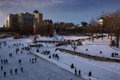 Large ice skating place, lots of people and buildings in the background