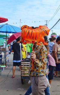 Woman holding balloon over face in city against sky