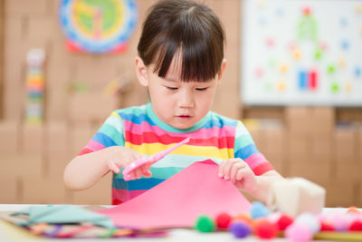 Young girl using scissors cutting papper for making craft for homeschooling