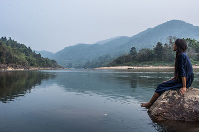 Rear view of woman relaxing on lake against clear sky