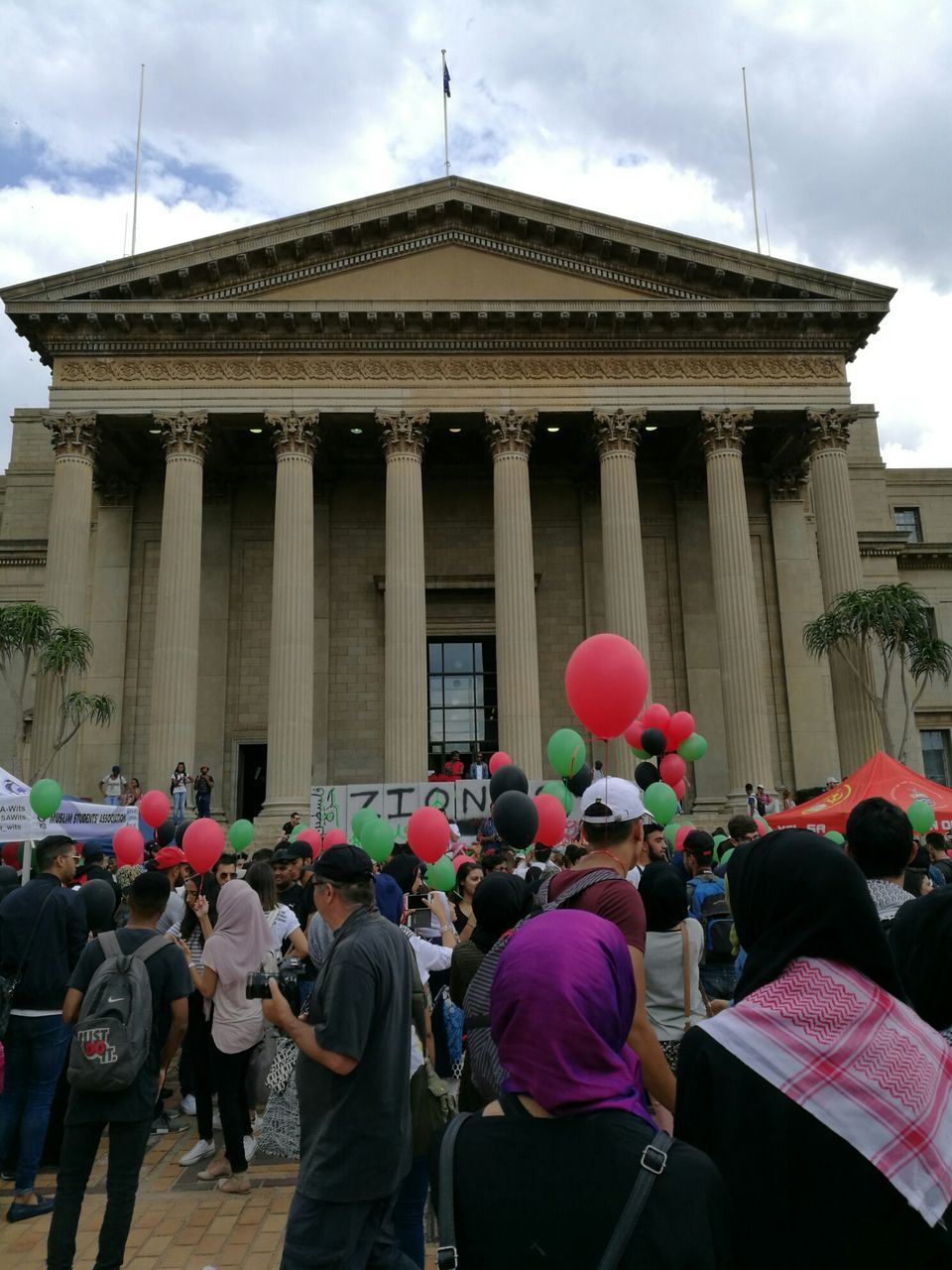 PEOPLE IN FRONT OF BUILDING AGAINST CLOUDY SKY