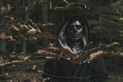 Close-up portrait of young man with spooky face paint in forest