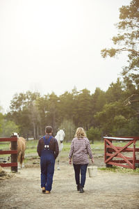 Rear view of farmers walking in farm against sky