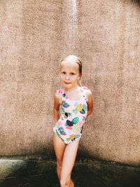 Portrait of cute girl standing below shower against wall