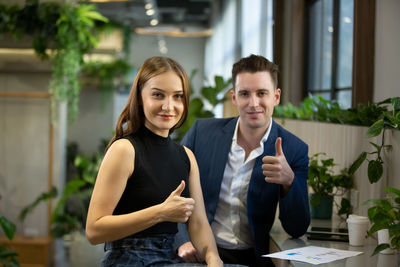 Portrait of smiling business people gesturing thumbs up while sitting at cafe