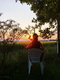 Rear view of man sitting on chair in field against sky