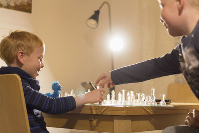 Brothers playing chess on table at home