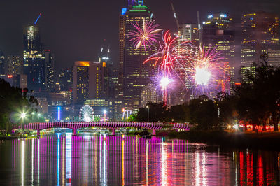 Firework display over river and illuminated buildings at night