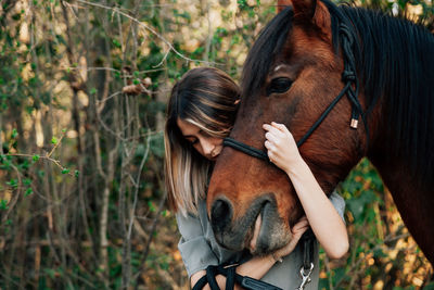 Young woman embracing horse while standing outdoors