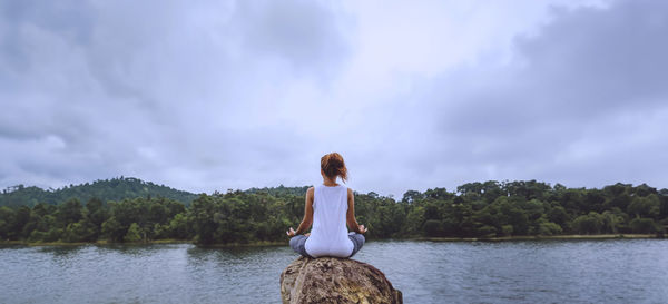 Rear view of woman standing by lake against sky