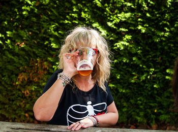 Woman drinking beer in glass against plants