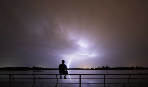 Silhouette man standing by railing against sky at night