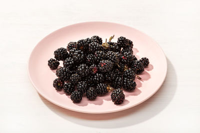 Fresh wild blackberries in plate on white wooden background. edible wild fruit