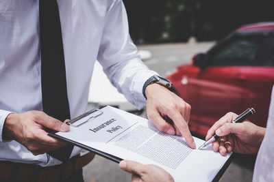 Midsection of customer signing contract while insurance agent holding clipboard