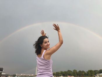 Rear view of woman gesturing against rainbow