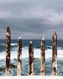 Weathered wooden fence at beach against sky