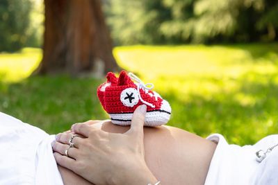 Midsection of pregnant woman with baby shoes on stomach lying in park