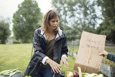 Mid adult woman standing by sign in vegetable garden