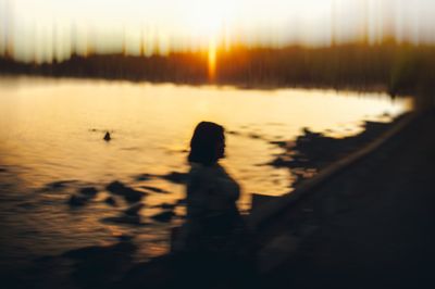 Silhouette person standing by lake against sky during sunset