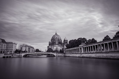 Bridge over river in city against cloudy sky