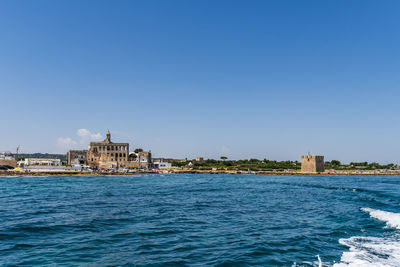 Sea by buildings against clear blue sky