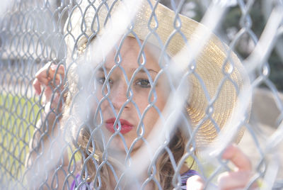 Portrait of young woman looking through chainlink fence