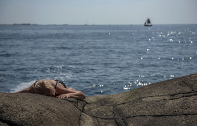 Woman lying on rocks by sea against sky