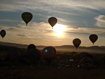 Hot air balloons flying over land against sky during sunset