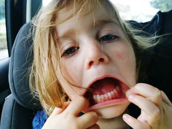 Close-up portrait of girl stretching mouth while traveling in car
