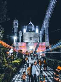 People walking on illuminated street amidst buildings at night