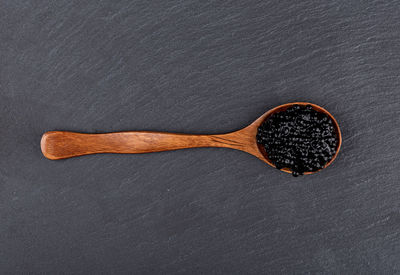 Top view of a wooden spoon with black caviar over a stone serving board.