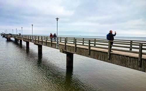 People on pier over sea against sky
