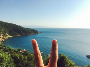 Close-up of hand against sea against clear sky