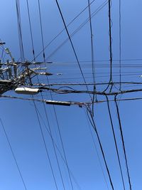 Low angle view of electricity pylons against clear blue sky