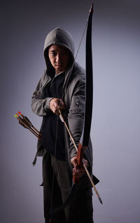 Mature man with bow and arrow standing against gray background